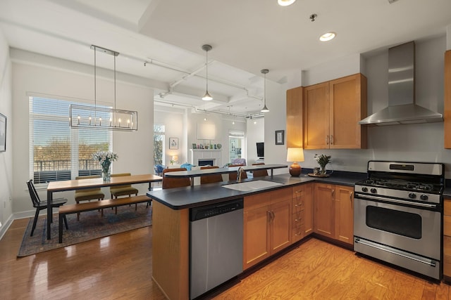 kitchen featuring dark countertops, appliances with stainless steel finishes, wall chimney range hood, a fireplace, and a sink