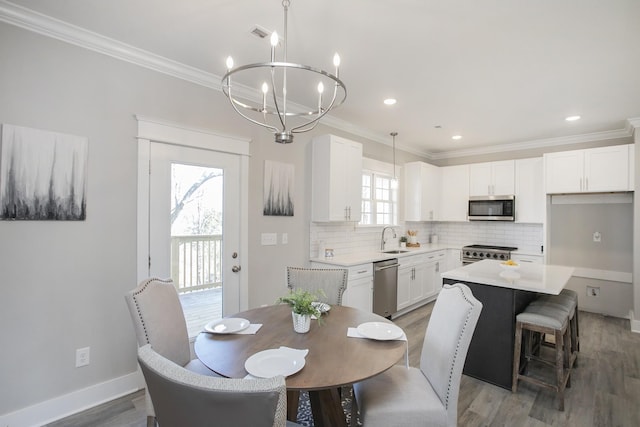 dining room featuring ornamental molding, light wood-type flooring, a chandelier, and baseboards