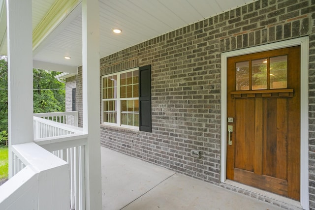 doorway to property featuring covered porch and brick siding