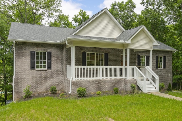 view of front of home with covered porch, brick siding, a front lawn, and roof with shingles