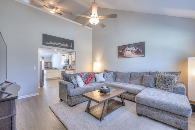 living area featuring high vaulted ceiling, light wood-type flooring, a ceiling fan, and baseboards