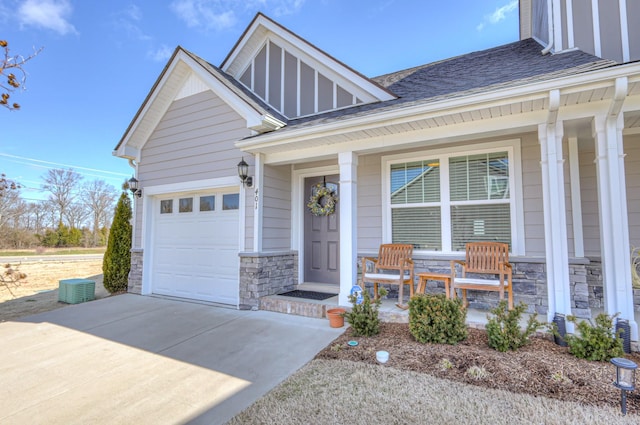 view of front of house with roof with shingles, a porch, a garage, stone siding, and driveway