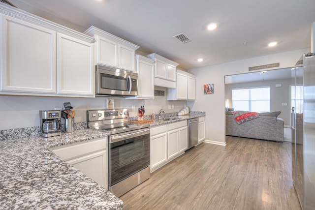 kitchen featuring light wood-style flooring, white cabinetry, stainless steel appliances, and open floor plan