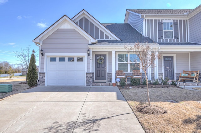 craftsman-style home featuring a garage, driveway, a shingled roof, stone siding, and covered porch