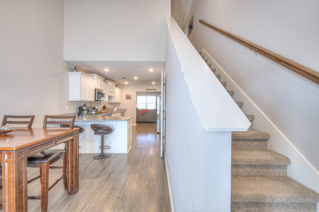 stairs with a high ceiling, wood finished floors, and recessed lighting