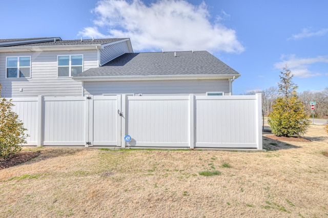 rear view of house featuring a shingled roof, a gate, fence, and a yard