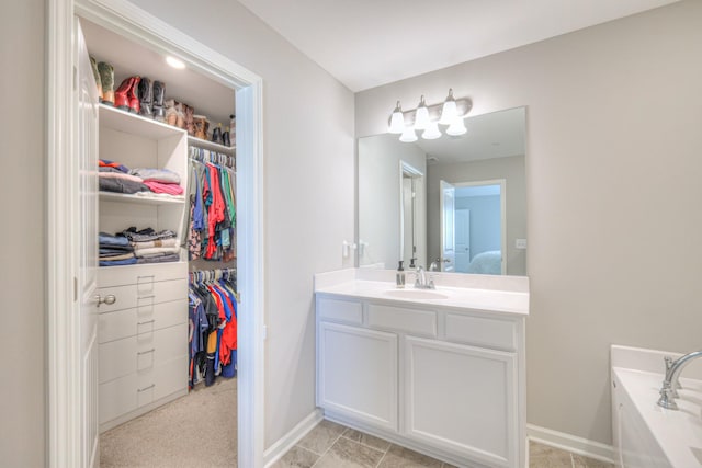 ensuite bathroom with a walk in closet, vanity, and baseboards