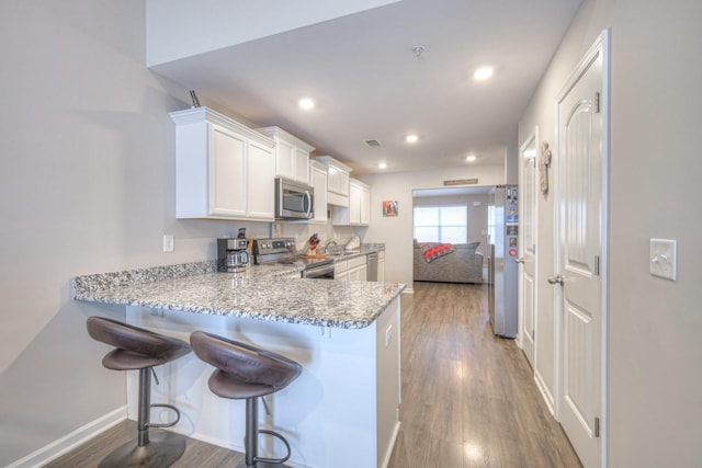 kitchen featuring stainless steel appliances, a peninsula, wood finished floors, and white cabinetry