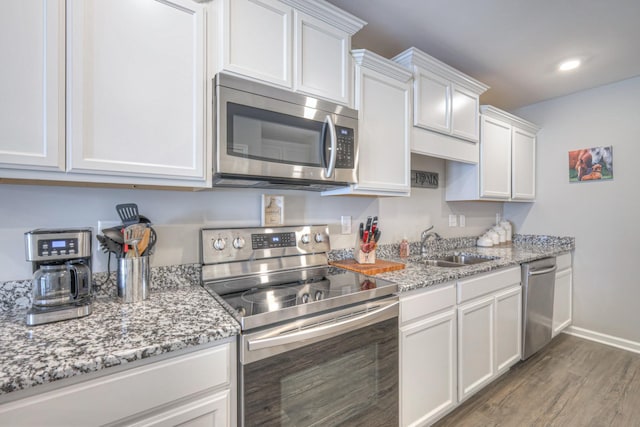 kitchen featuring baseboards, white cabinets, appliances with stainless steel finishes, wood finished floors, and a sink