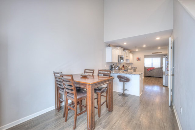 dining space with a high ceiling, recessed lighting, wood finished floors, and baseboards