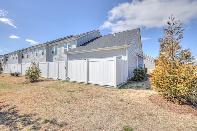 view of side of property with a yard, fence, and a shingled roof