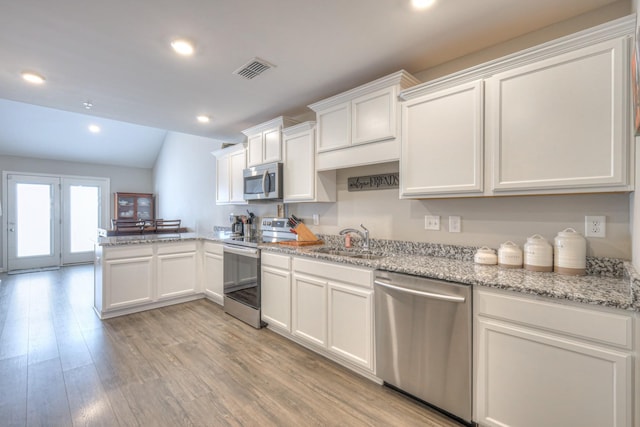 kitchen with stainless steel appliances, a peninsula, a sink, white cabinetry, and light wood-style floors