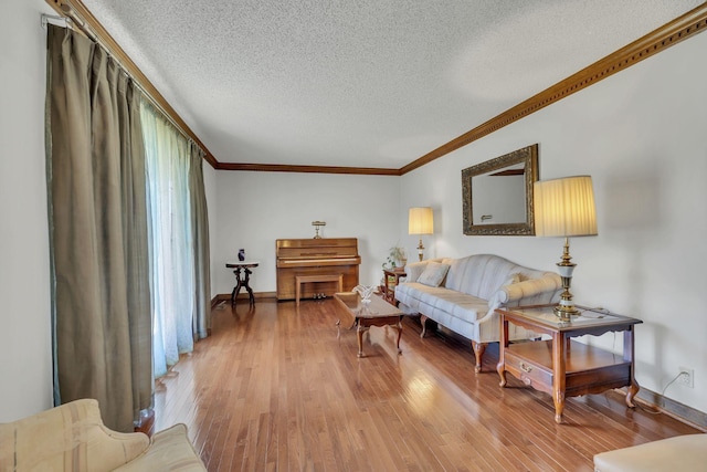 living area featuring ornamental molding, light wood-type flooring, a textured ceiling, and baseboards