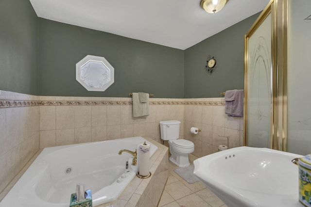 bathroom featuring toilet, a tub with jets, tile walls, and tile patterned floors