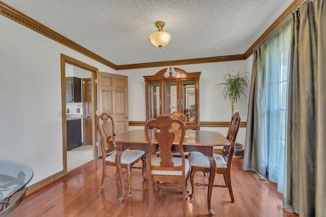 dining space featuring light wood-style flooring, a textured ceiling, visible vents, and crown molding