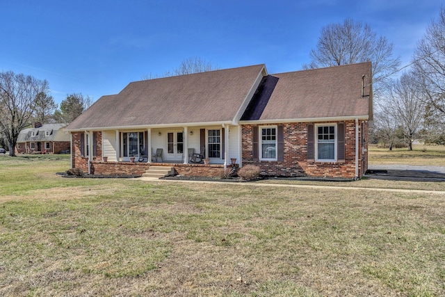 view of front of property featuring a porch, a front yard, brick siding, and roof with shingles