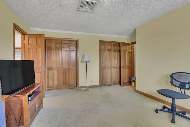 interior space with a textured ceiling, carpet floors, visible vents, baseboards, and two closets