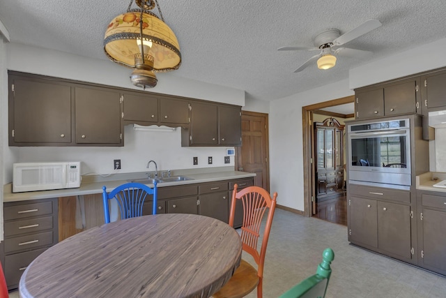 kitchen with light floors, light countertops, white microwave, a textured ceiling, and oven