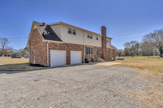 exterior space with driveway, a garage, a chimney, and brick siding