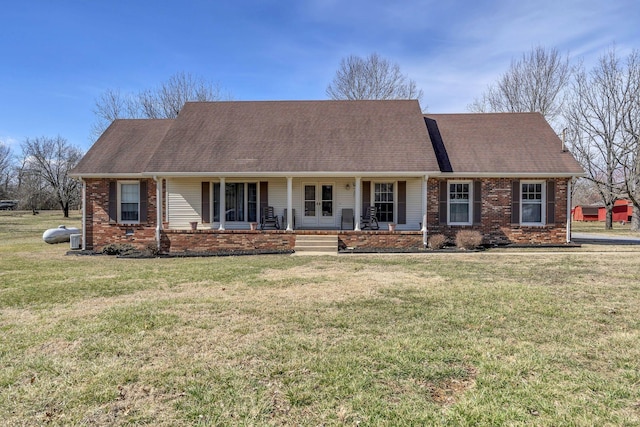 view of front of house with a shingled roof, a front yard, covered porch, and brick siding