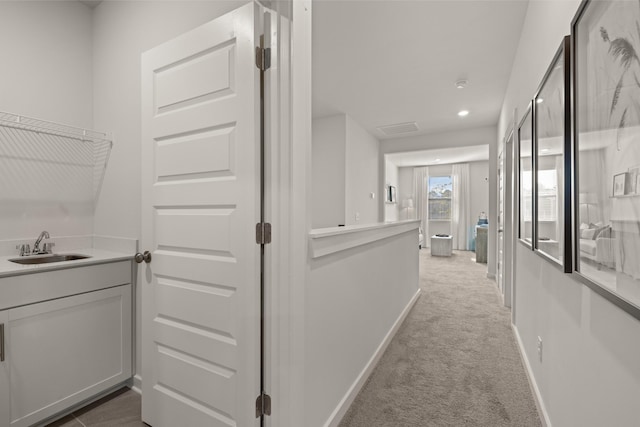 hall with baseboards, recessed lighting, a sink, and light colored carpet