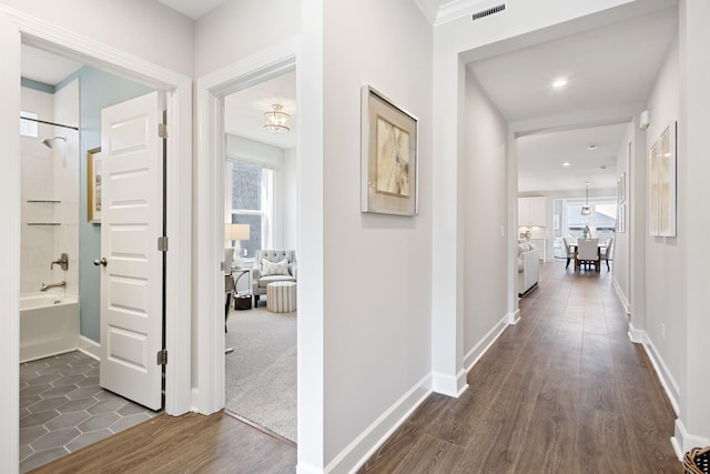 hallway with dark wood-type flooring, plenty of natural light, visible vents, and baseboards