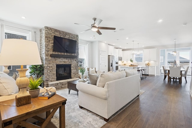 living room with a ceiling fan, recessed lighting, dark wood-style flooring, and a stone fireplace