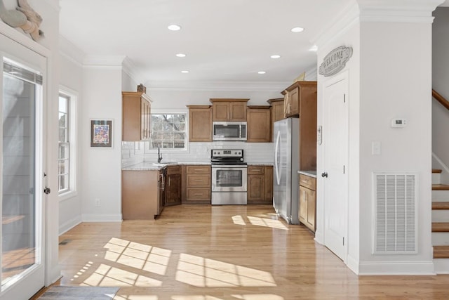 kitchen with visible vents, brown cabinetry, appliances with stainless steel finishes, light wood-type flooring, and backsplash