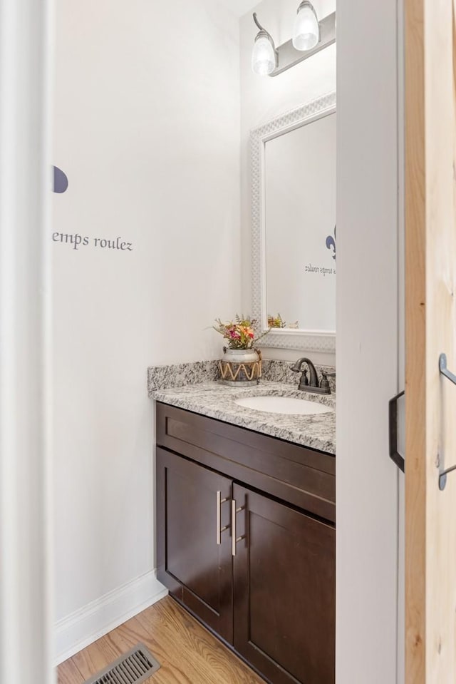 bathroom with visible vents, vanity, baseboards, and wood finished floors