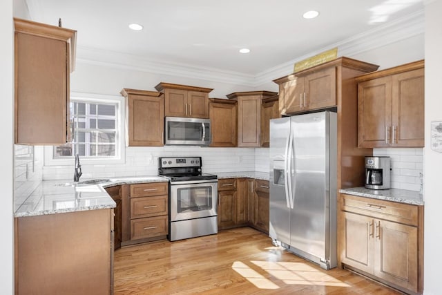 kitchen featuring brown cabinets, light stone countertops, stainless steel appliances, light wood-style floors, and a sink