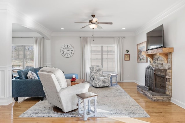 living room featuring ornamental molding, a stone fireplace, light wood finished floors, and ceiling fan