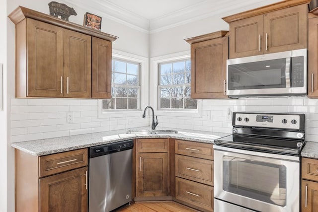 kitchen featuring stainless steel appliances, light stone counters, a sink, and crown molding