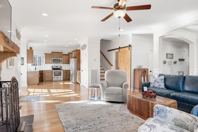 living area with ceiling fan, a barn door, light wood-style flooring, recessed lighting, and ornamental molding