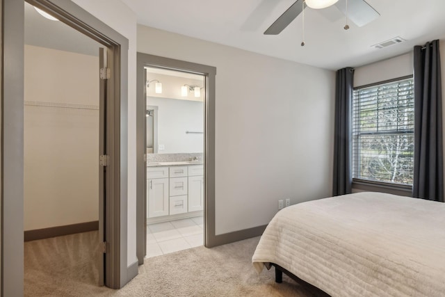 bedroom with light carpet, visible vents, baseboards, a ceiling fan, and ensuite bath