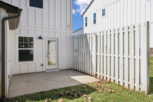 property entrance with board and batten siding, a patio area, and fence