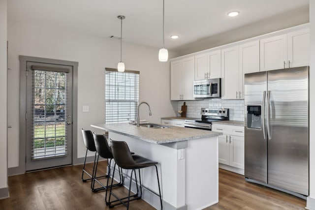 kitchen with an island with sink, dark wood-style floors, a sink, stainless steel appliances, and backsplash