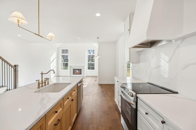 kitchen featuring premium range hood, a sink, appliances with stainless steel finishes, a glass covered fireplace, and pendant lighting