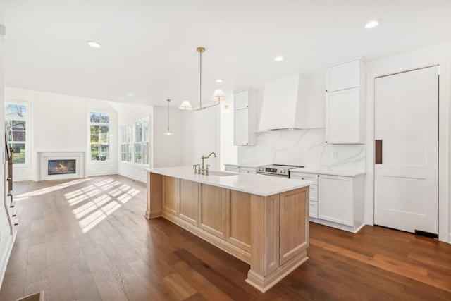 kitchen featuring tasteful backsplash, electric range, a glass covered fireplace, a sink, and premium range hood