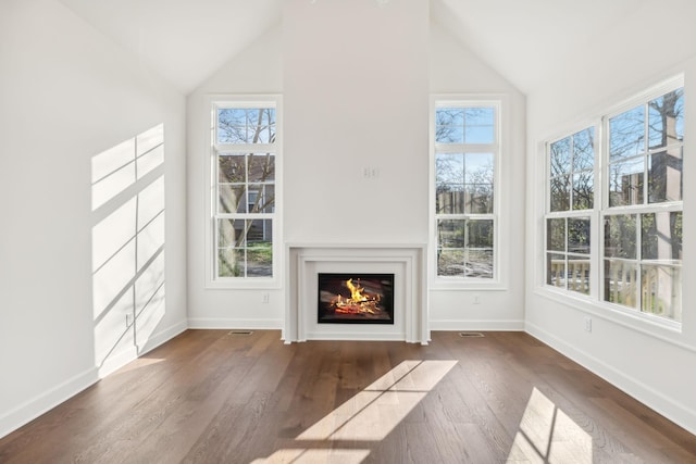 unfurnished living room featuring vaulted ceiling, a warm lit fireplace, wood finished floors, and a wealth of natural light