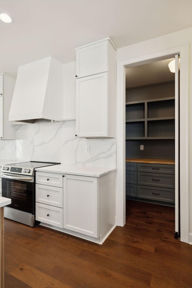 kitchen featuring custom exhaust hood, light countertops, dark wood-type flooring, white cabinets, and stainless steel range with electric stovetop