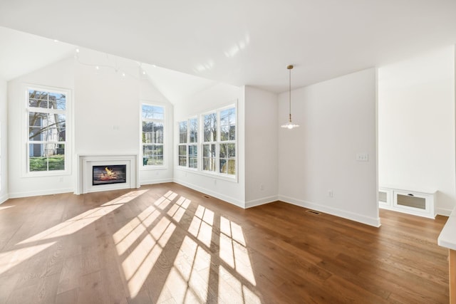 unfurnished living room with hardwood / wood-style flooring, baseboards, vaulted ceiling, and a glass covered fireplace