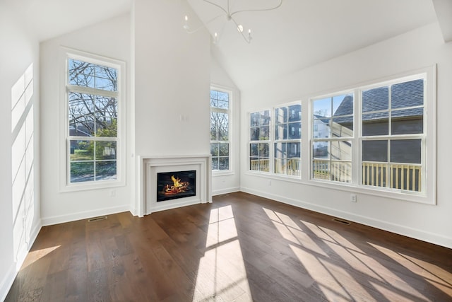 unfurnished living room featuring a healthy amount of sunlight, visible vents, wood finished floors, and a glass covered fireplace