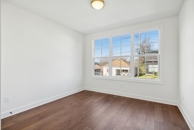 empty room featuring visible vents, baseboards, and dark wood-style flooring