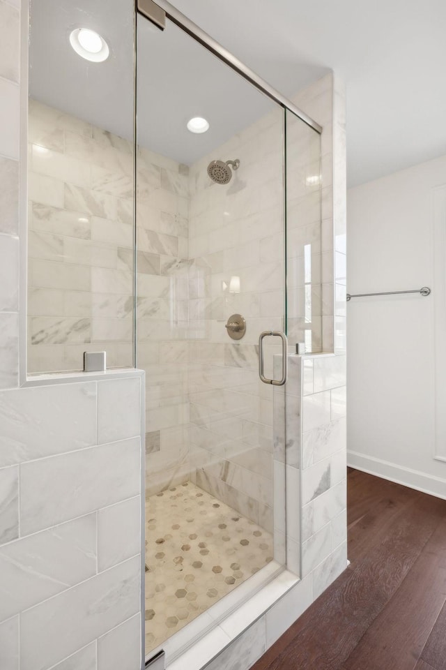 bathroom featuring wood finished floors, a shower stall, and baseboards