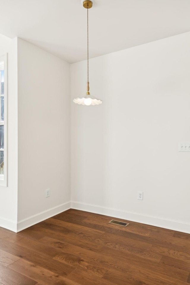 unfurnished room featuring dark wood-type flooring, visible vents, and baseboards