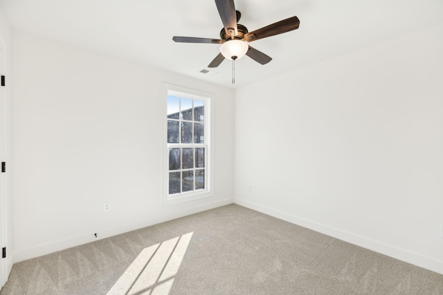 spare room featuring light colored carpet, ceiling fan, visible vents, and baseboards