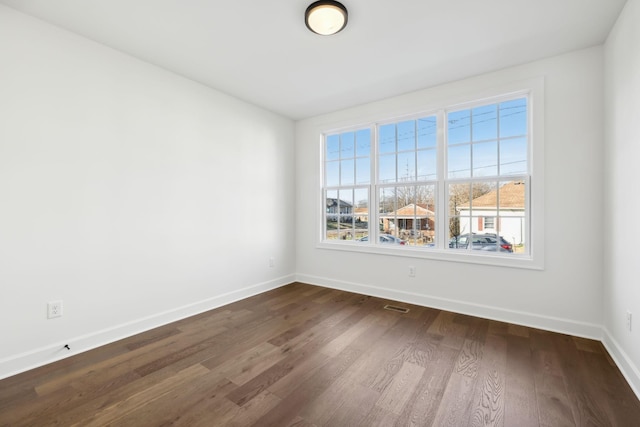 spare room with dark wood-style floors, visible vents, and baseboards