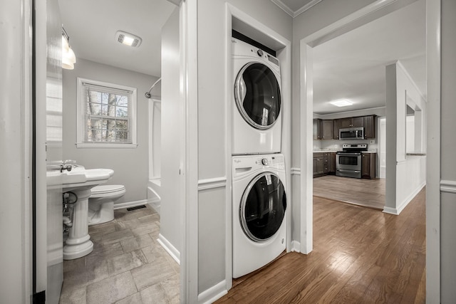 laundry area with crown molding, stacked washing maching and dryer, wood finished floors, laundry area, and baseboards