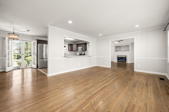 unfurnished living room featuring crown molding, visible vents, a glass covered fireplace, wood finished floors, and ceiling fan with notable chandelier