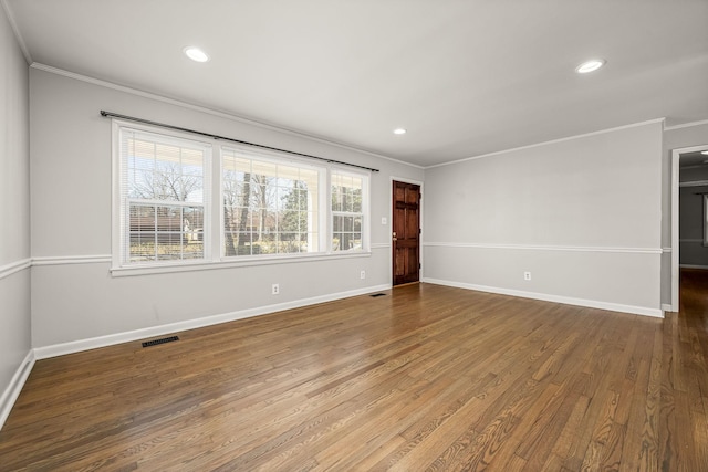 empty room featuring baseboards, visible vents, wood finished floors, and ornamental molding